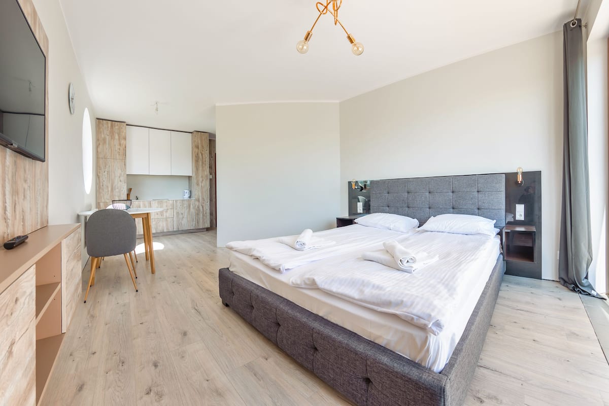 A modern hotel room with a large bed, a desk, and a kitchenette.