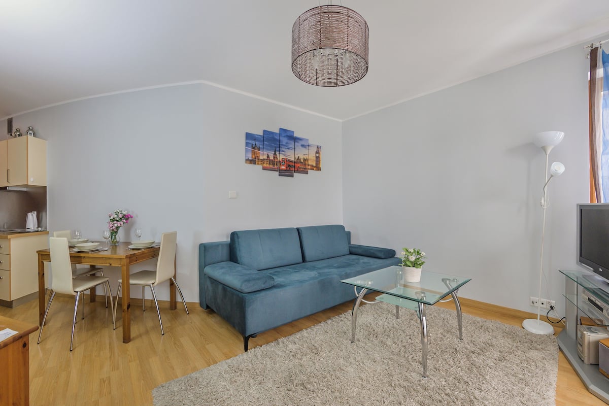 A modern living room with a blue sofa, a glass coffee table, and a TV stand.