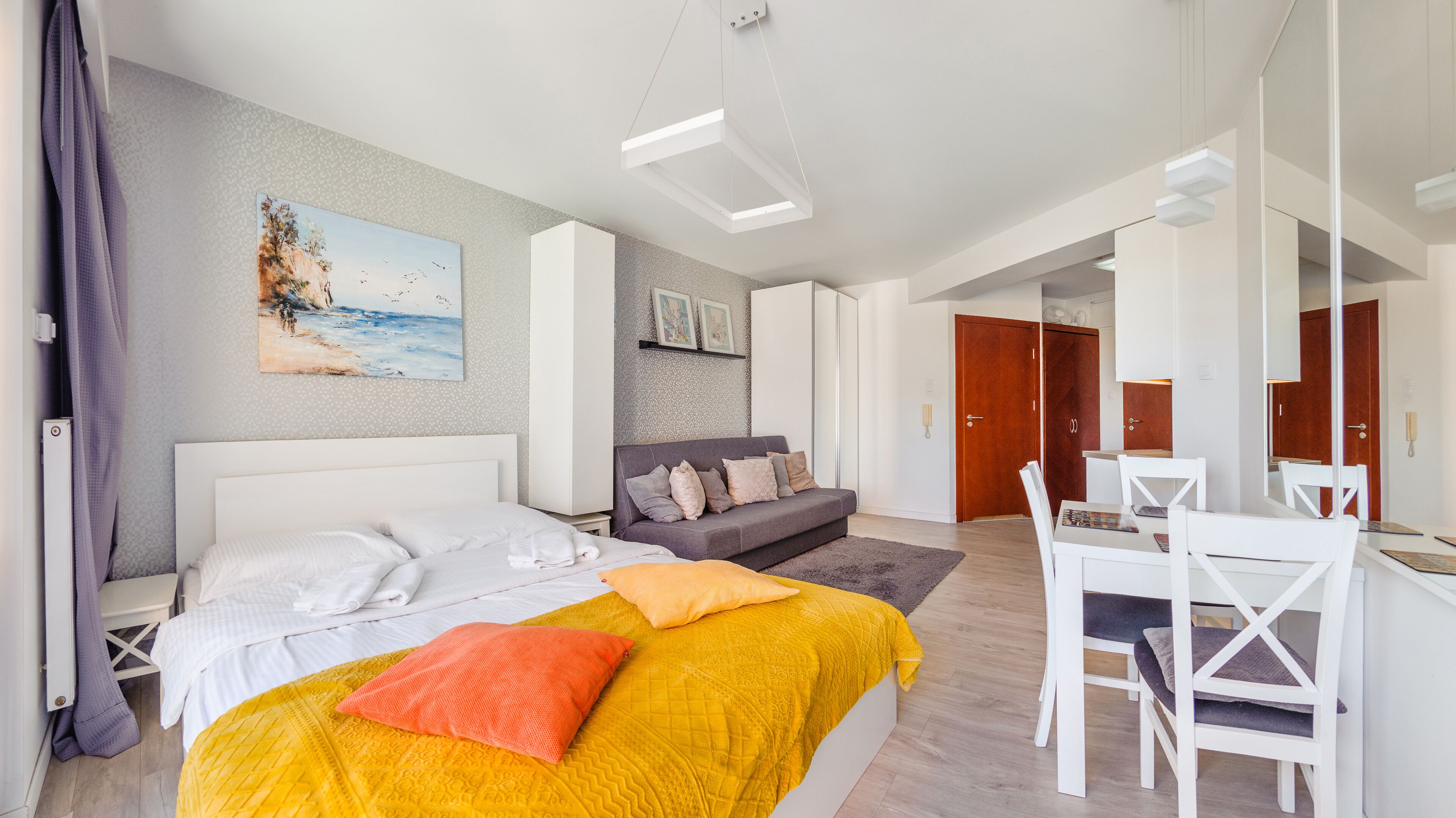 A modern hotel room with a bed, a sofa, a dining table, and a painting on the wall.