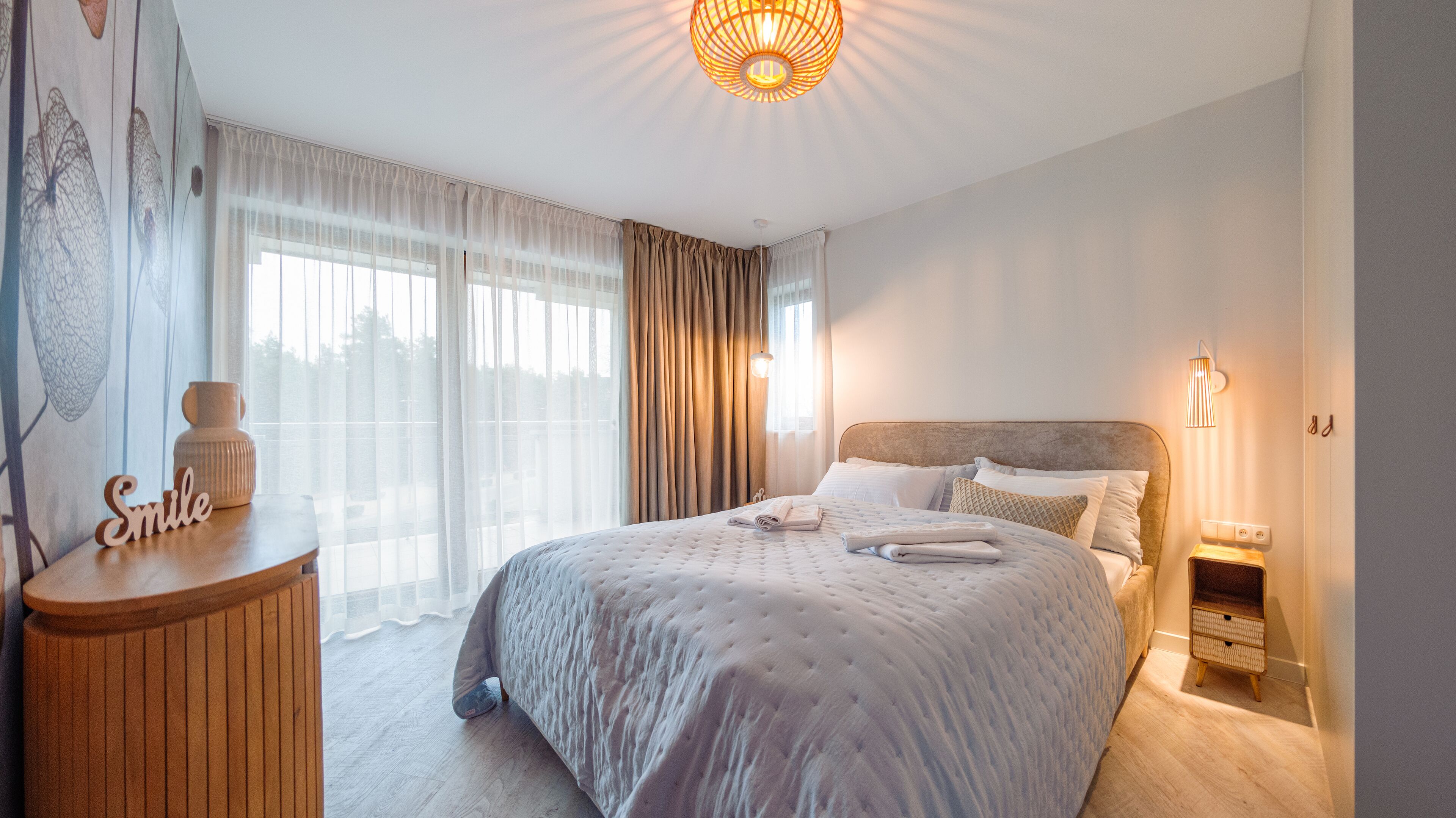 A bedroom with a large bed, a bedside table, a nightstand, and a wall-mounted lamp.