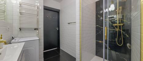 Un baño moderno con un lavamanos blanco, un inodoro, una ducha con puertas de vidrio y una puerta que da a otra habitación.