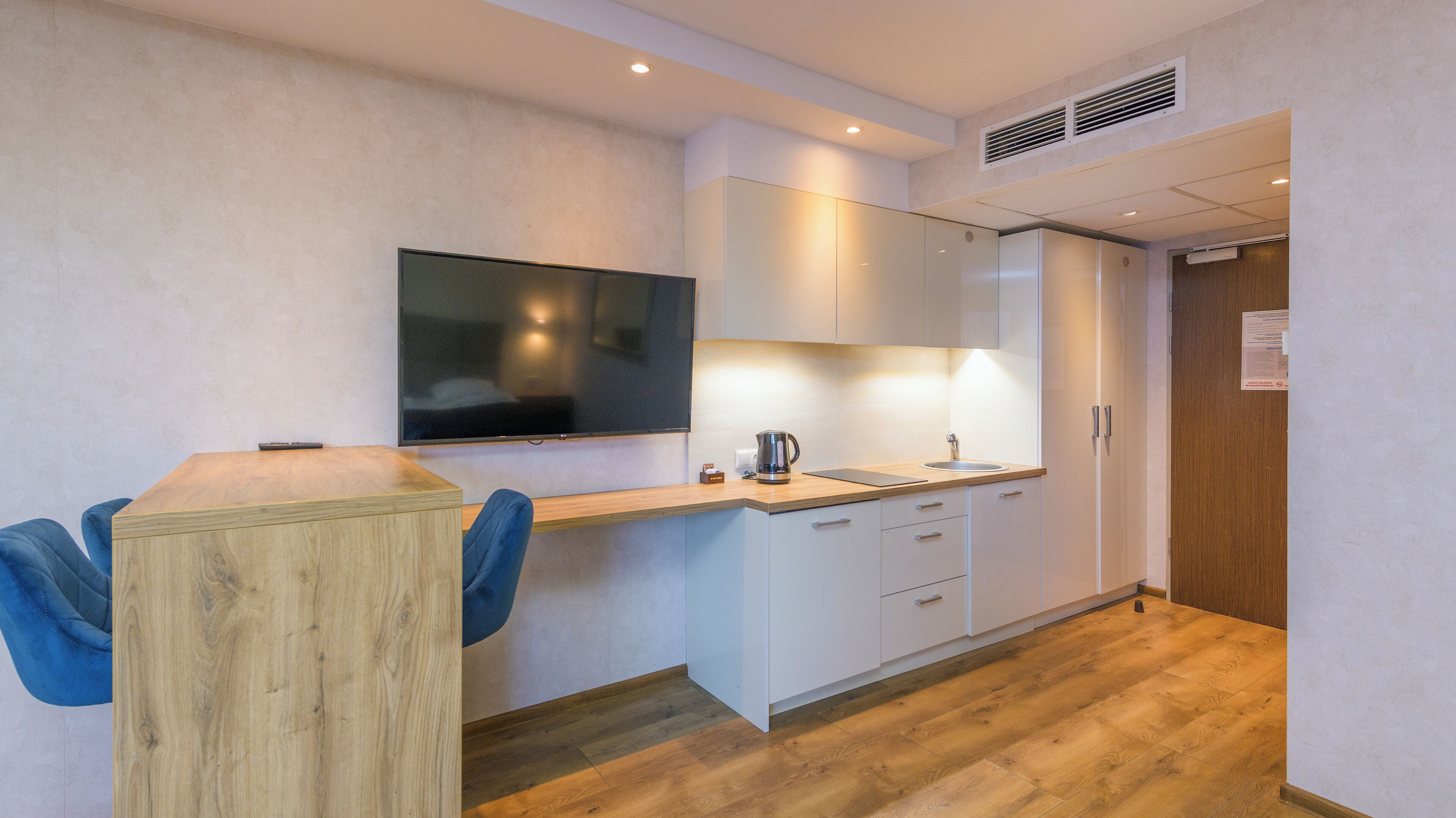 Eine moderne Küche mit Holztisch, Flachbildfernseher, weißen Schränken und einer Kaffeemaschine.