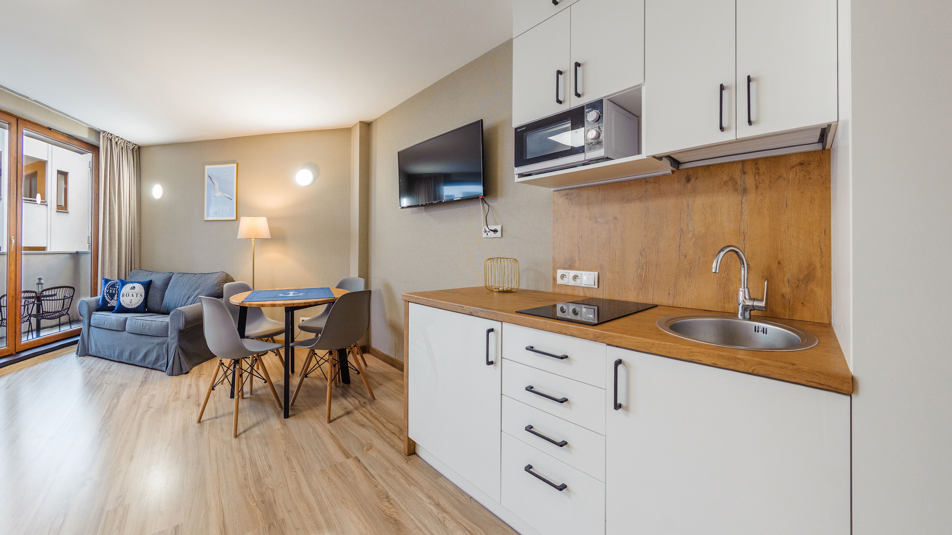 A modern kitchen with a wooden countertop, a built-in microwave, and a sink. There is a dining area with a table and chairs, and a sofa in the living area.