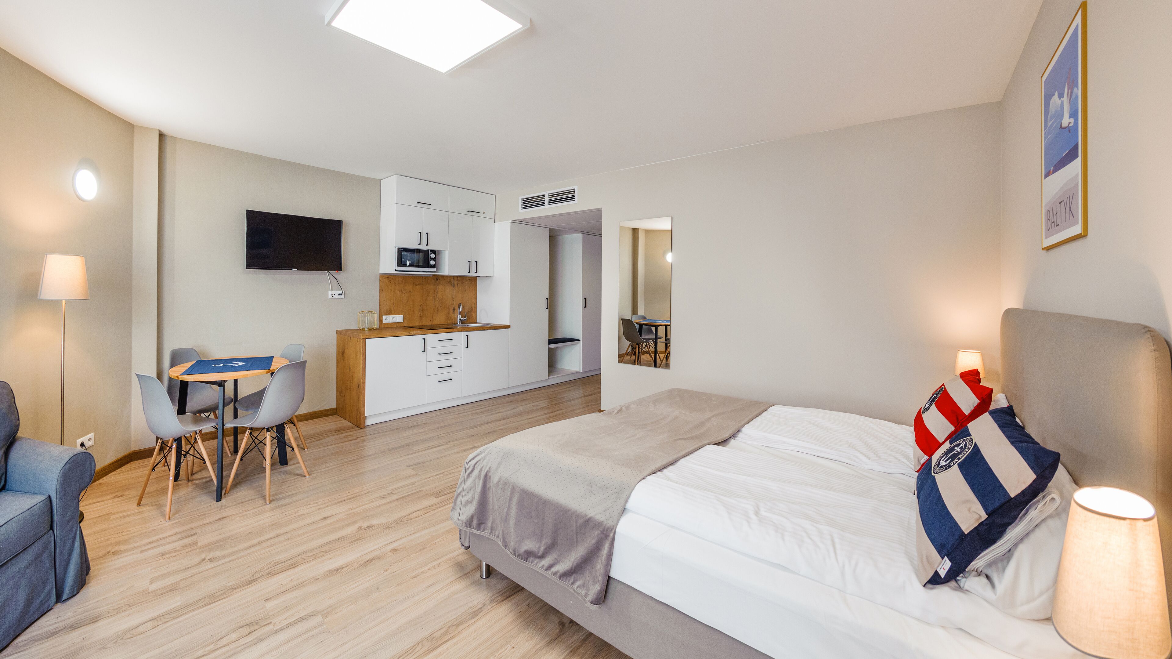 Una habitación de hotel moderna con cama, escritorio, silla, kitchenette pequeña y televisión.