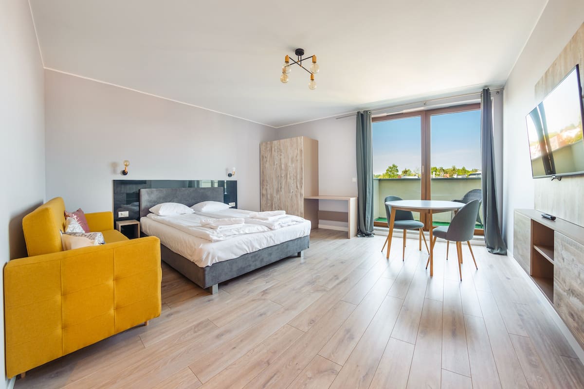 A modern hotel room with a bed, a yellow armchair, a desk, and a dining table.