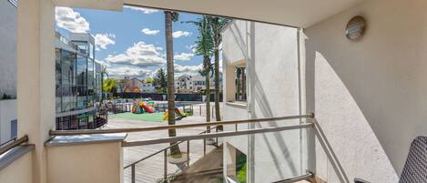 A balcony with a view of a playground, a white wall, and a patterned chair.