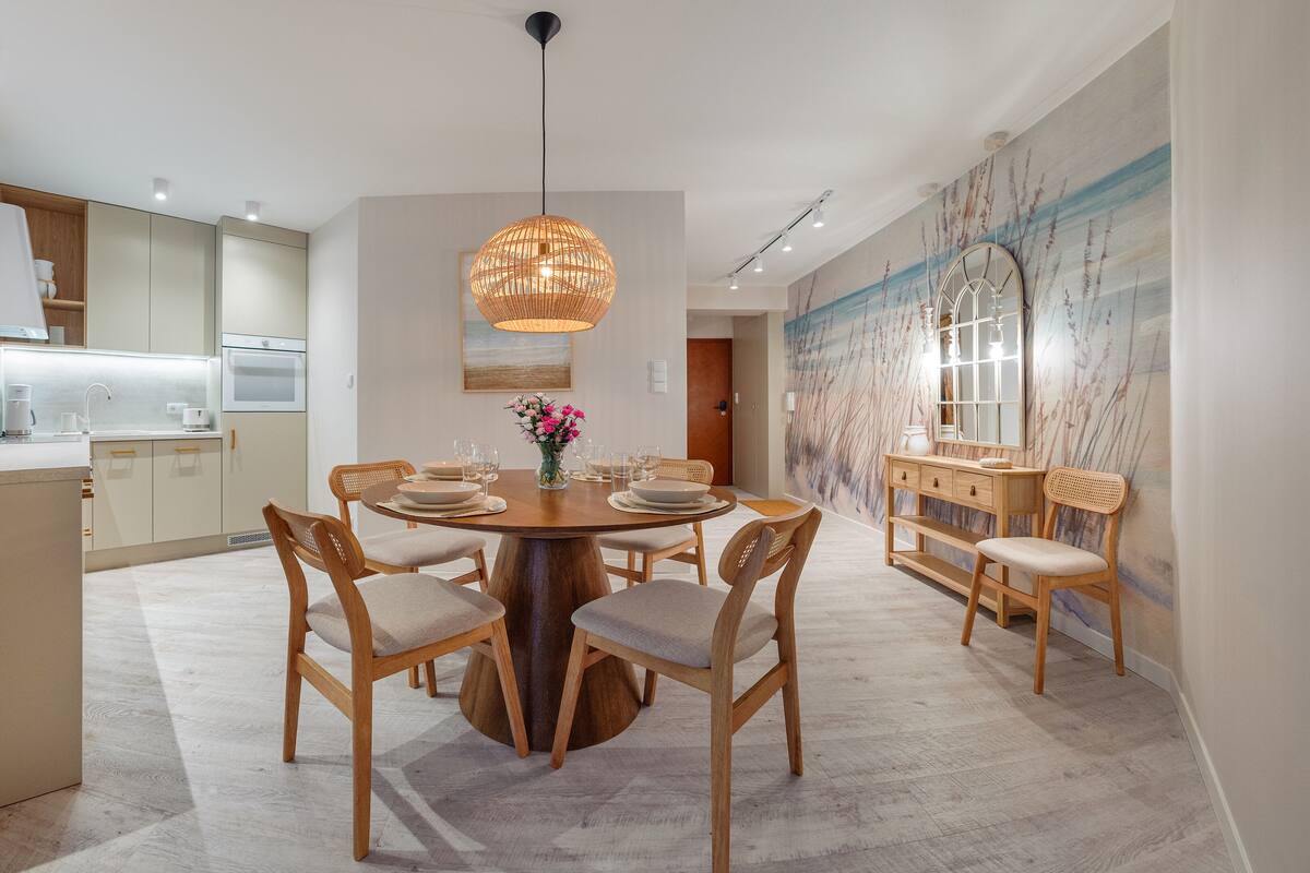 A modern dining room with a round wooden table, six chairs, and a hanging light fixture.