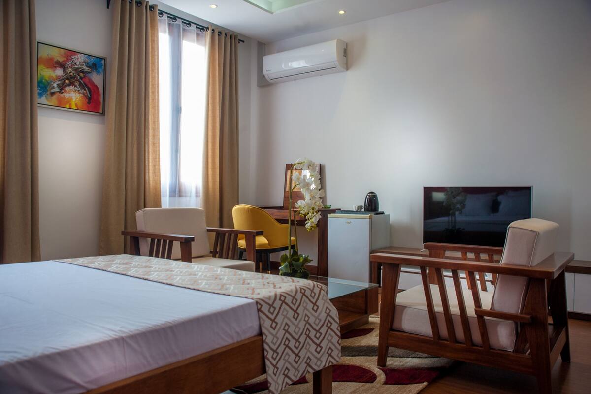A hotel room with a bed, a desk, a chair, a television, and an air conditioning unit.