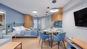 A modern hotel room with a bed, a dining area with chairs and a table, a TV, and a wooden floor. - Apartamenty Sun&Snow Na Klifie (Wladyslawowo)