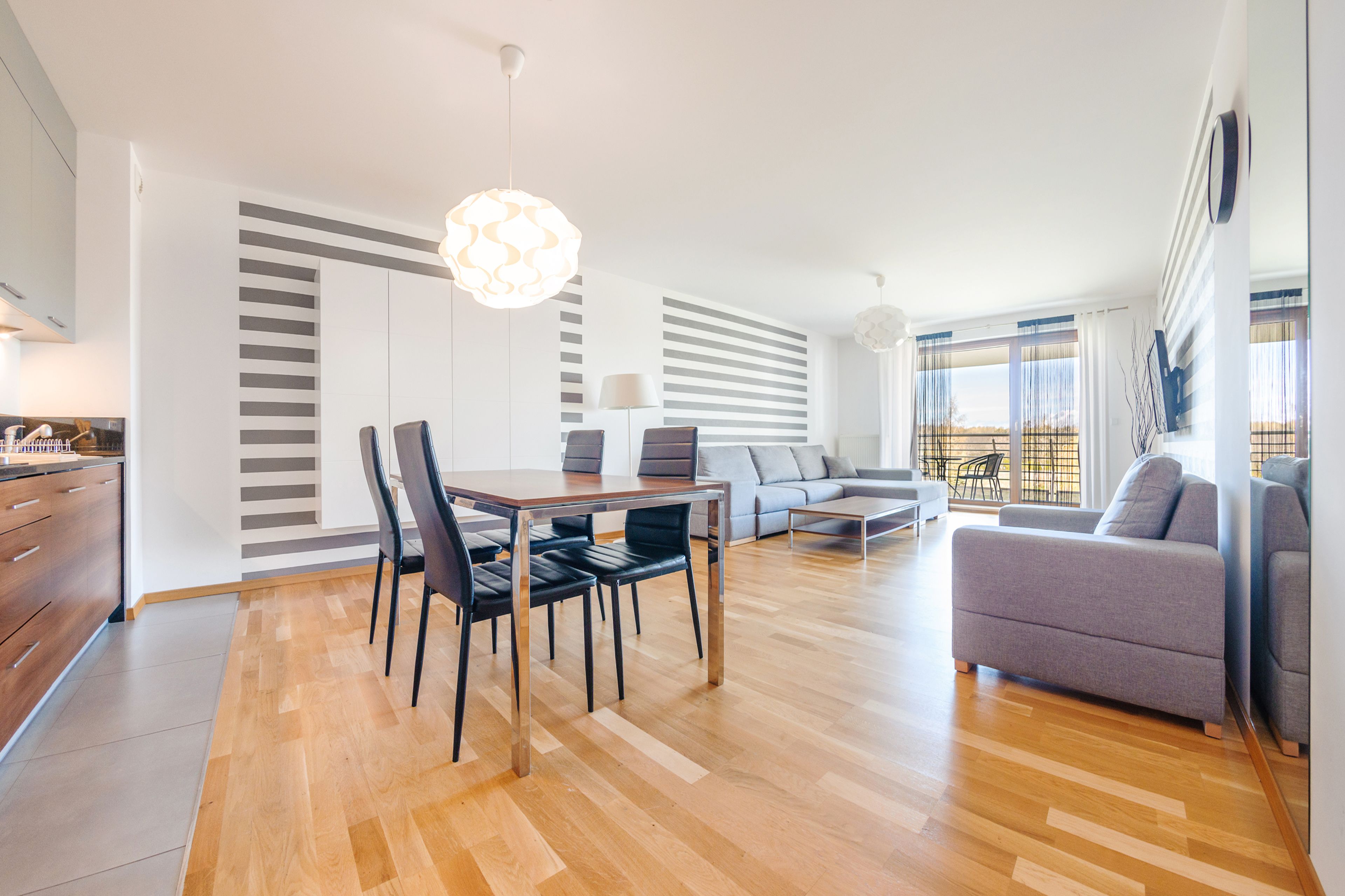 Una sala de estar moderna con comedor, que presenta piso de madera, un sofá, una mesa de centro y una mesa de comedor con sillas.