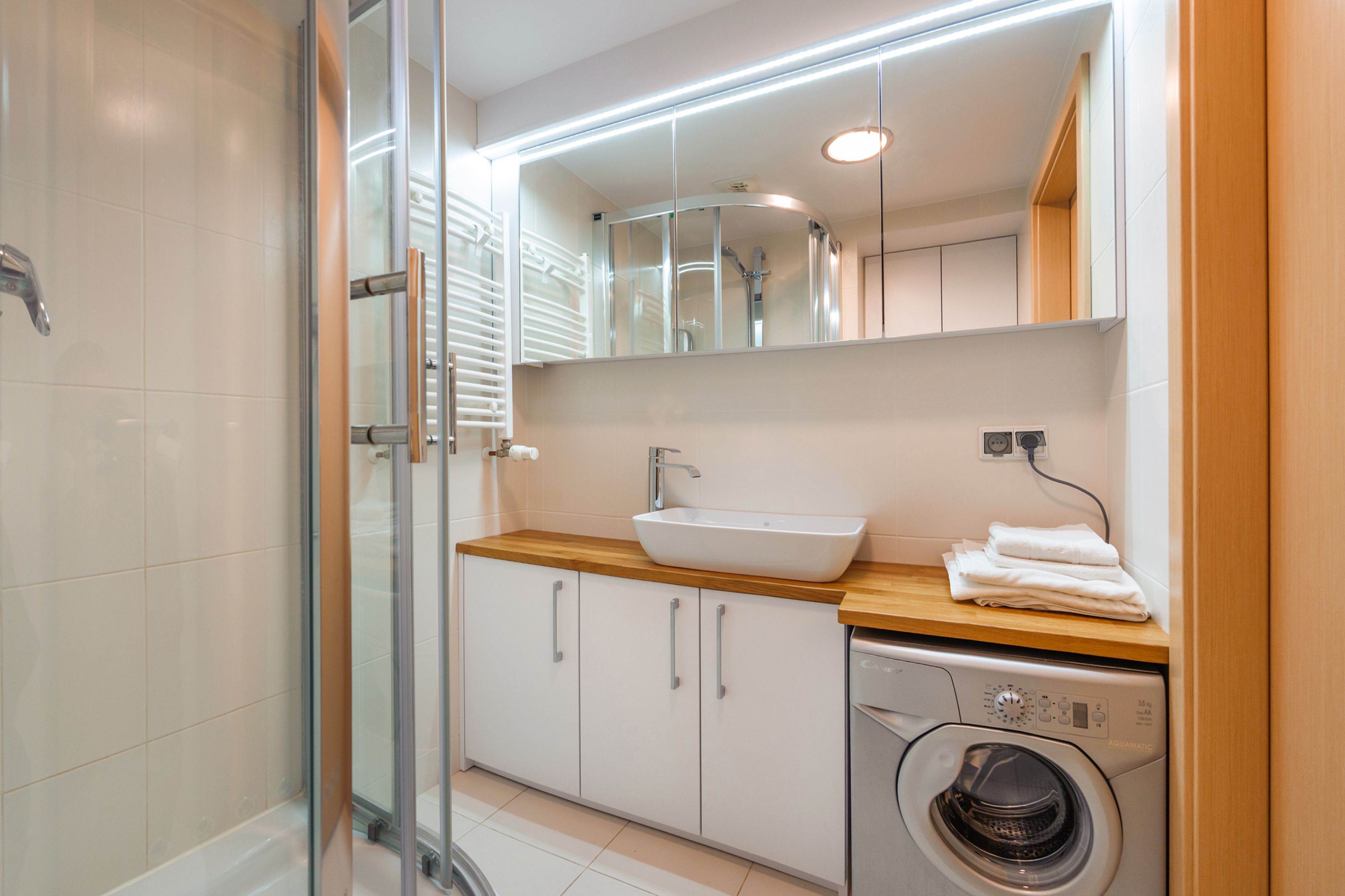 A modern bathroom with a glass shower enclosure, a white sink, and a built-in washing machine.