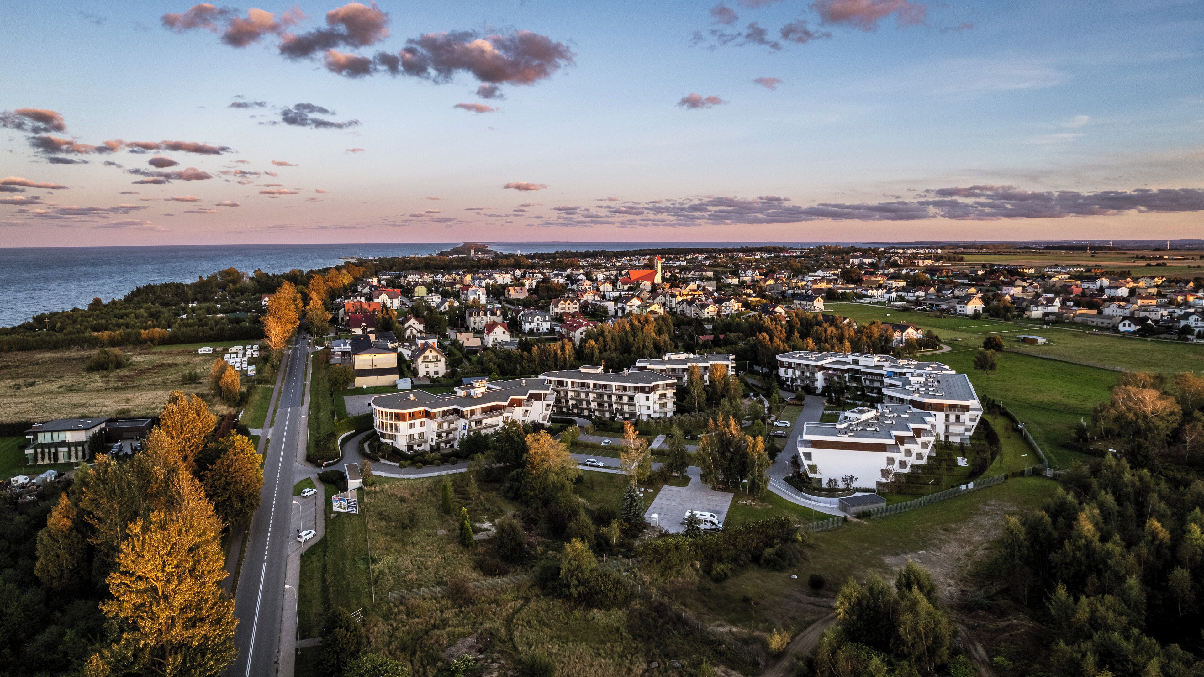 Ett flygbildsfoto av ett bostadsområde med hus, en väg och en vattenyta i bakgrunden.