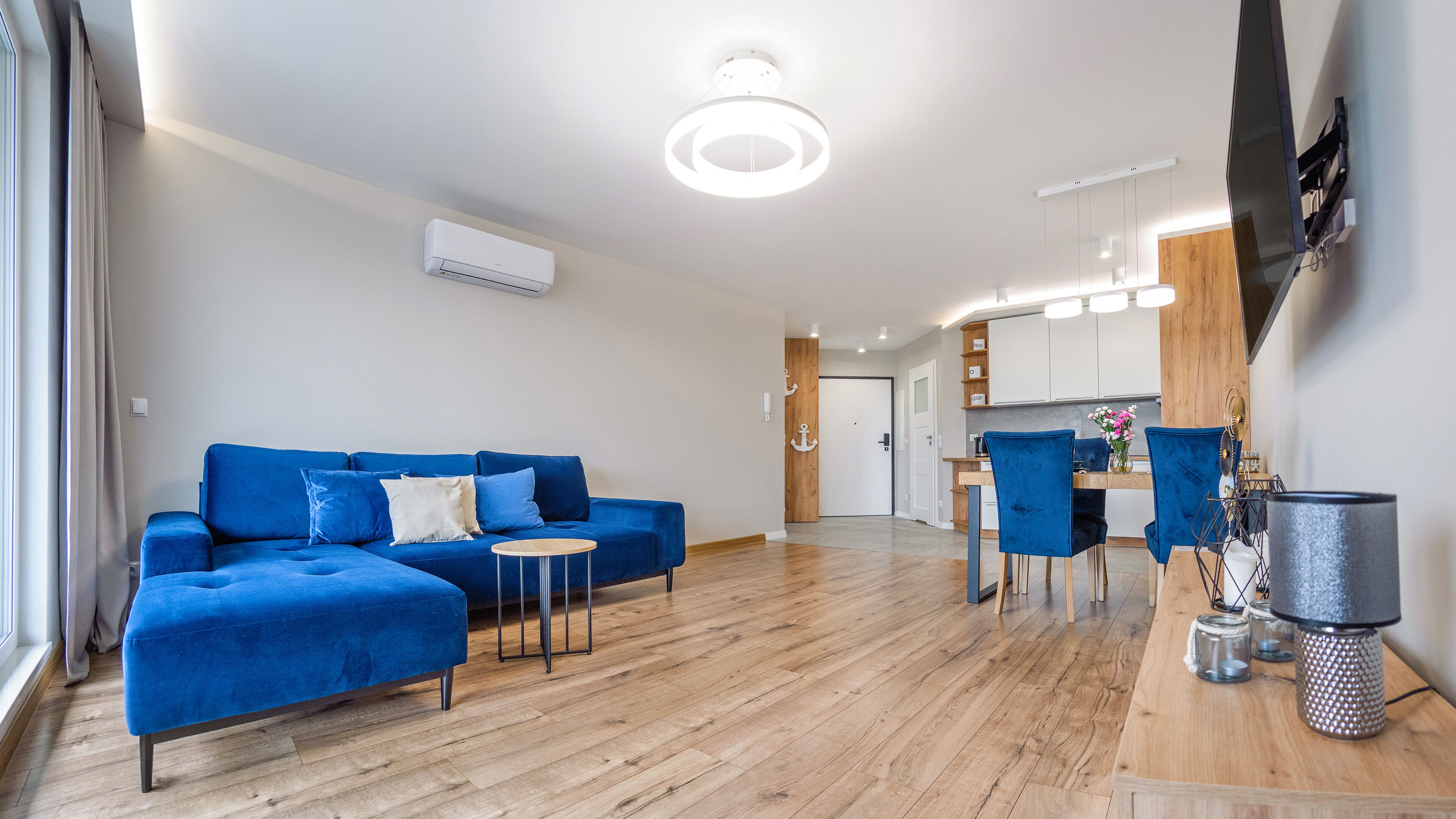 Un salon moderne avec un canapé bleu, une petite table ronde et un coin repas avec des chaises bleues.