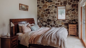 Un dormitorio con pared de piedra, una cama de madera, una mesita de noche, una lámpara y un aparador.