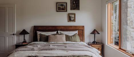 Une chambre à coucher avec une tête de lit en bois, un lit recouvert d’une couverture à rayures, deux tables de chevet avec des lampes et trois tableaux encadrés accrochés au mur.
