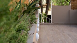 Un espacio exterior moderno con una terraza de madera, barandilla blanca y abundante vegetación.