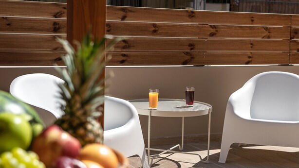 Una terraza de madera con una mesa, dos sillas, una cesta de frutas y dos vasos de jugo.