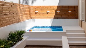 Un área pequeña y privada con hidromasaje, con escalones de acceso, rodeada por un muro de madera y escalones blancos.