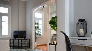 Una sala de estar moderna con una televisión, un escritorio y una silla. Hay plantas y una lámpara decorativa en el escritorio.