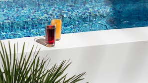 Escena a la piscina amb dues copes de beguda sobre una superfície blanca.
