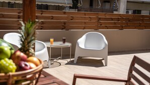 Una terraza de madera con una mesa, dos sillas blancas y una cesta de frutas.