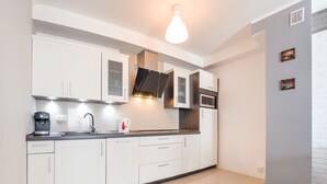 A modern kitchen with white cabinets, a coffee machine, and a built-in oven. - Apartamenty Sun & Snow Rybacka (Wladyslawowo)