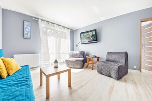 Una sala de estar moderna con un sofá azul, un sillón gris, una mesa de centro de madera y un televisor en la pared.