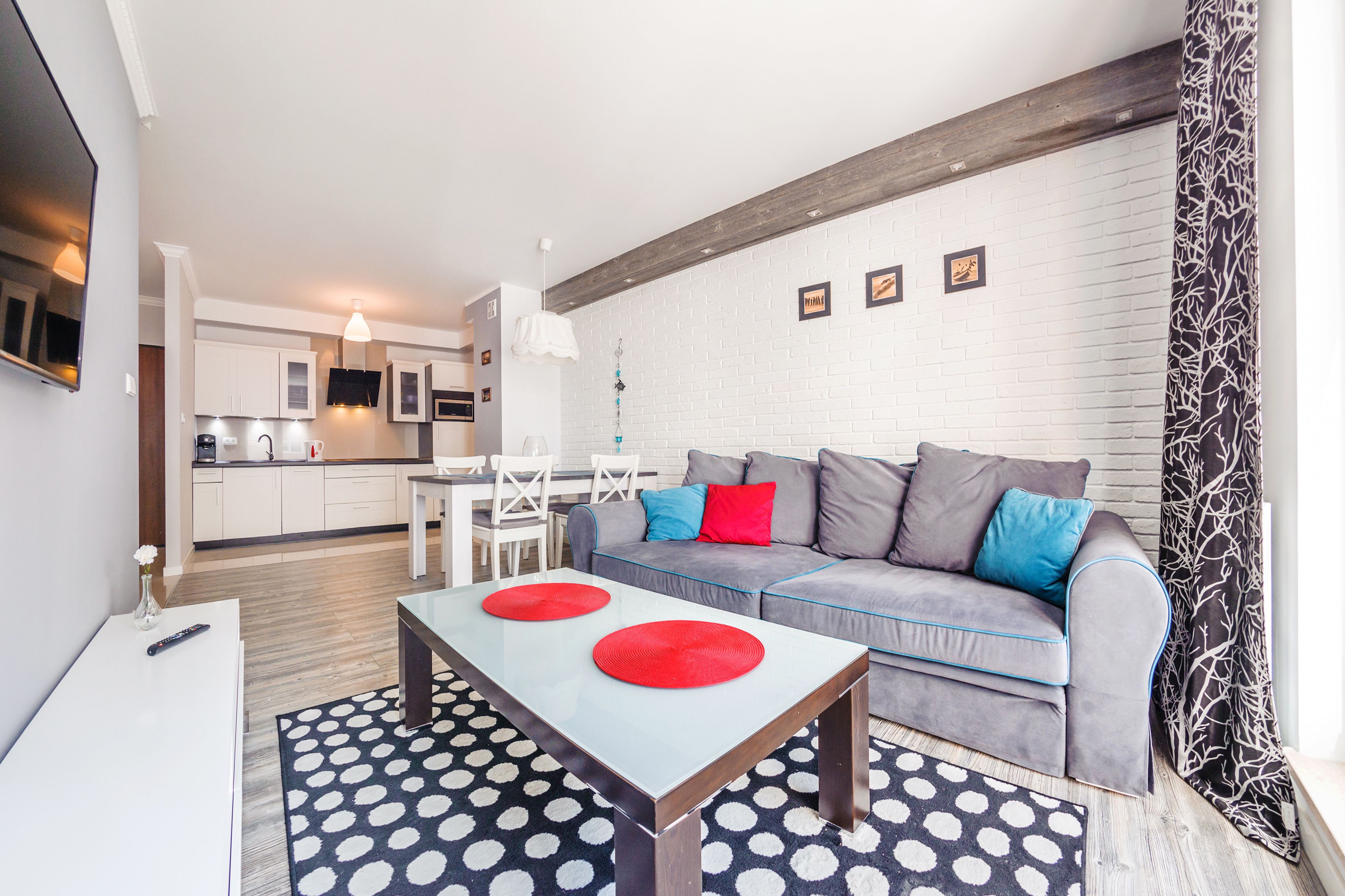 A modern living room with a grey sofa, a coffee table, and a dining area with a white table and chairs.