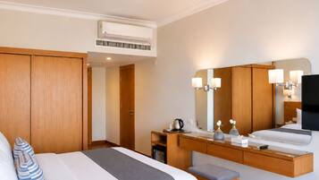 A hotel room with a bed, a desk, a chair, a mirror, and an air conditioning unit.