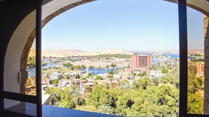 A view through an arched window of a cityscape with buildings, greenery, and a river. - Basma Executive Club (Aswan)