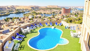 A rooftop pool with blue lounge chairs and a view of a cityscape and river. - Basma Executive Club (Aswan)