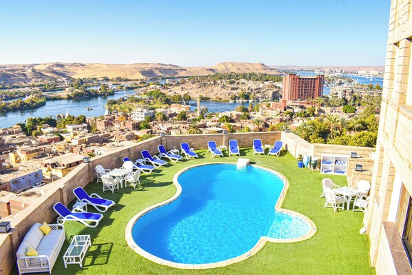 A rooftop pool with blue lounge chairs and a view of a cityscape and river. - Basma Executive Club (Aswan)