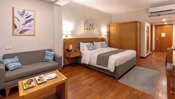 A hotel room with a bed, a sofa, a nightstand, a desk, and a small table with fruit.