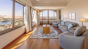 A spacious living room with a large window, a sofa, a coffee table, and a view of a cityscape. - Basma Executive Club (Aswan)