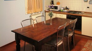 A dining area with a wooden table and chairs, a window with curtains, a kitchen with a stove and microwave, and a blue ceiling. - Venezianamente - Casa del Batelo (Venice)