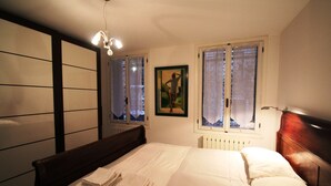A bedroom with a bed, a headboard, a window with curtains, a radiator, and a wall with a painting. - Venezianamente - Casa dell'Orio (Venice)