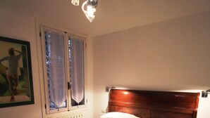 A bedroom with a wooden bed, a radiator, a window with curtains, and a painting on the wall. - Venezianamente - Casa dell'Orio (Venice)