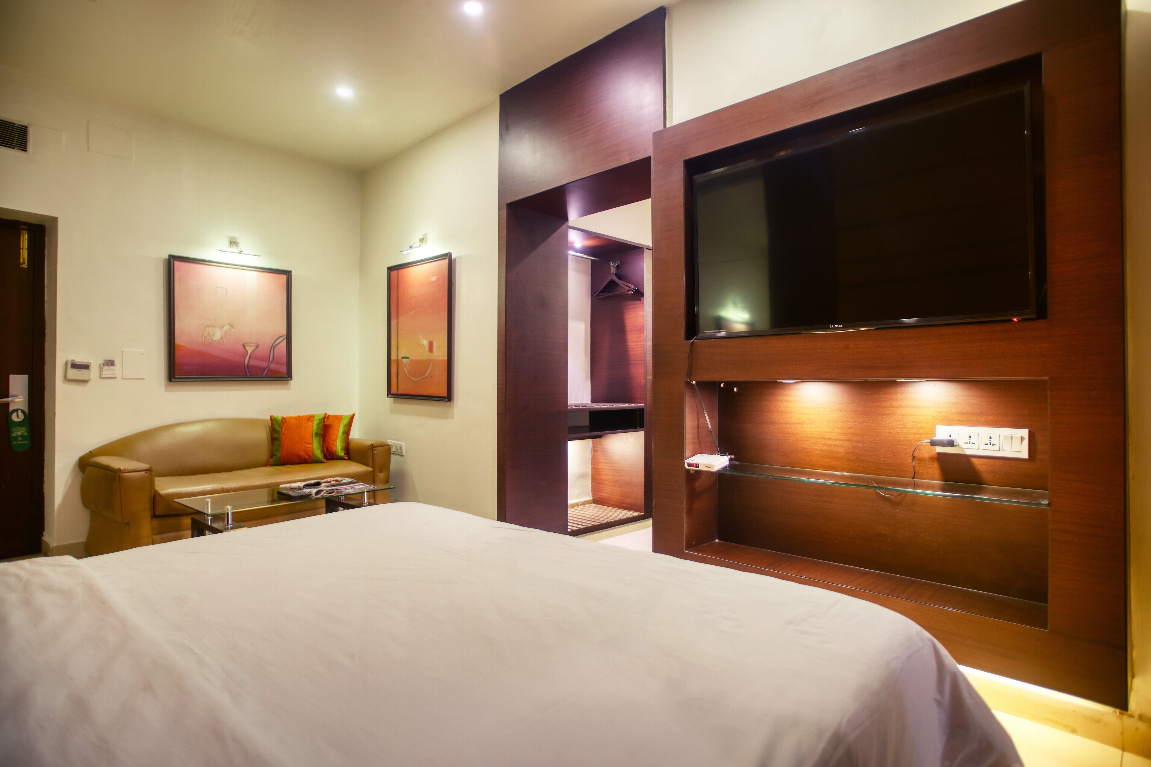 A hotel room with a large bed, a wooden wardrobe with a TV, a coat rack, and a painting on the wall.