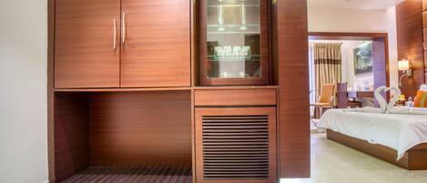 A hotel room with a large wardrobe, a glass display cabinet, a bed, and a ceiling fan.