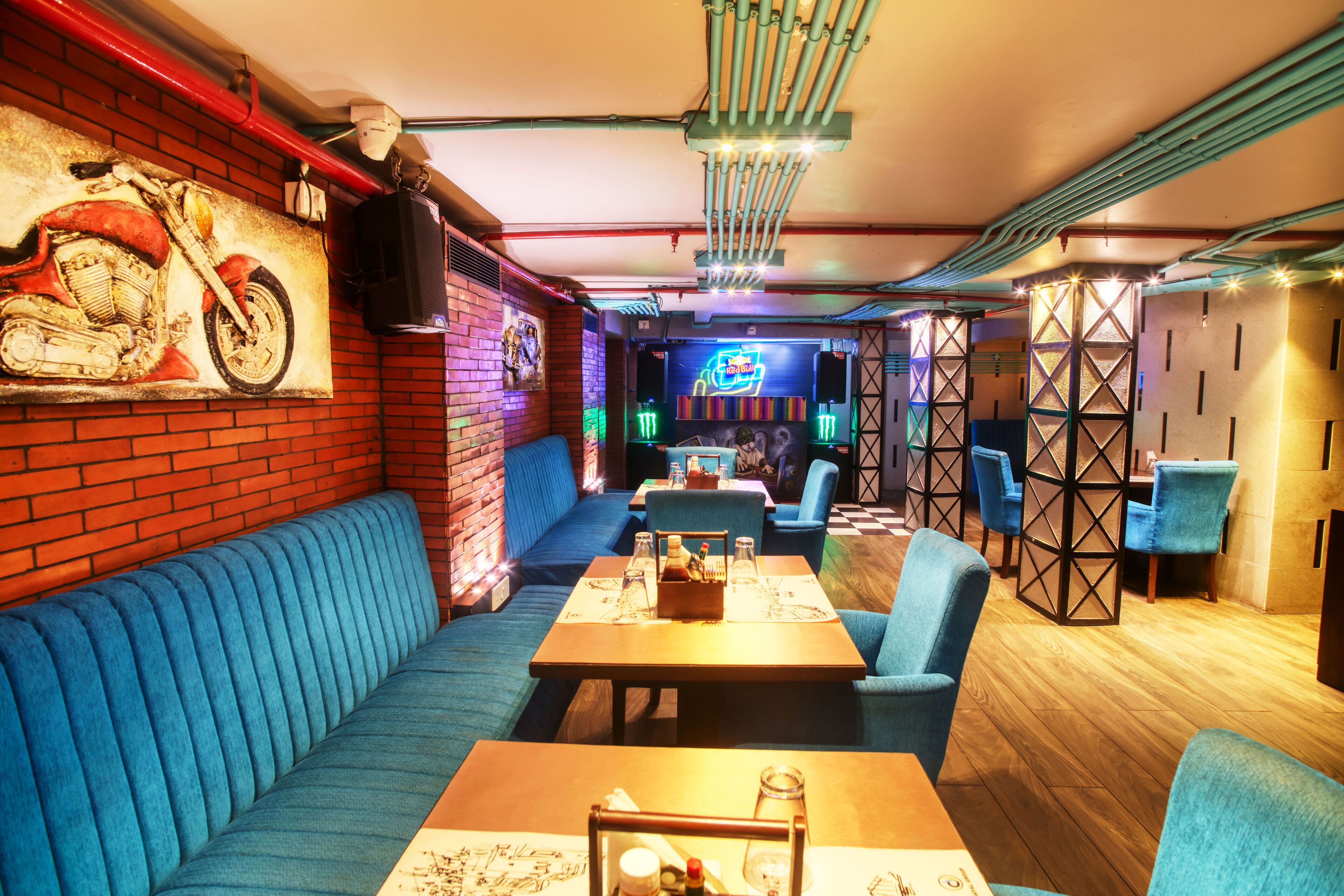 A restaurant with blue upholstered booths, wooden tables, and a neon sign in the background.