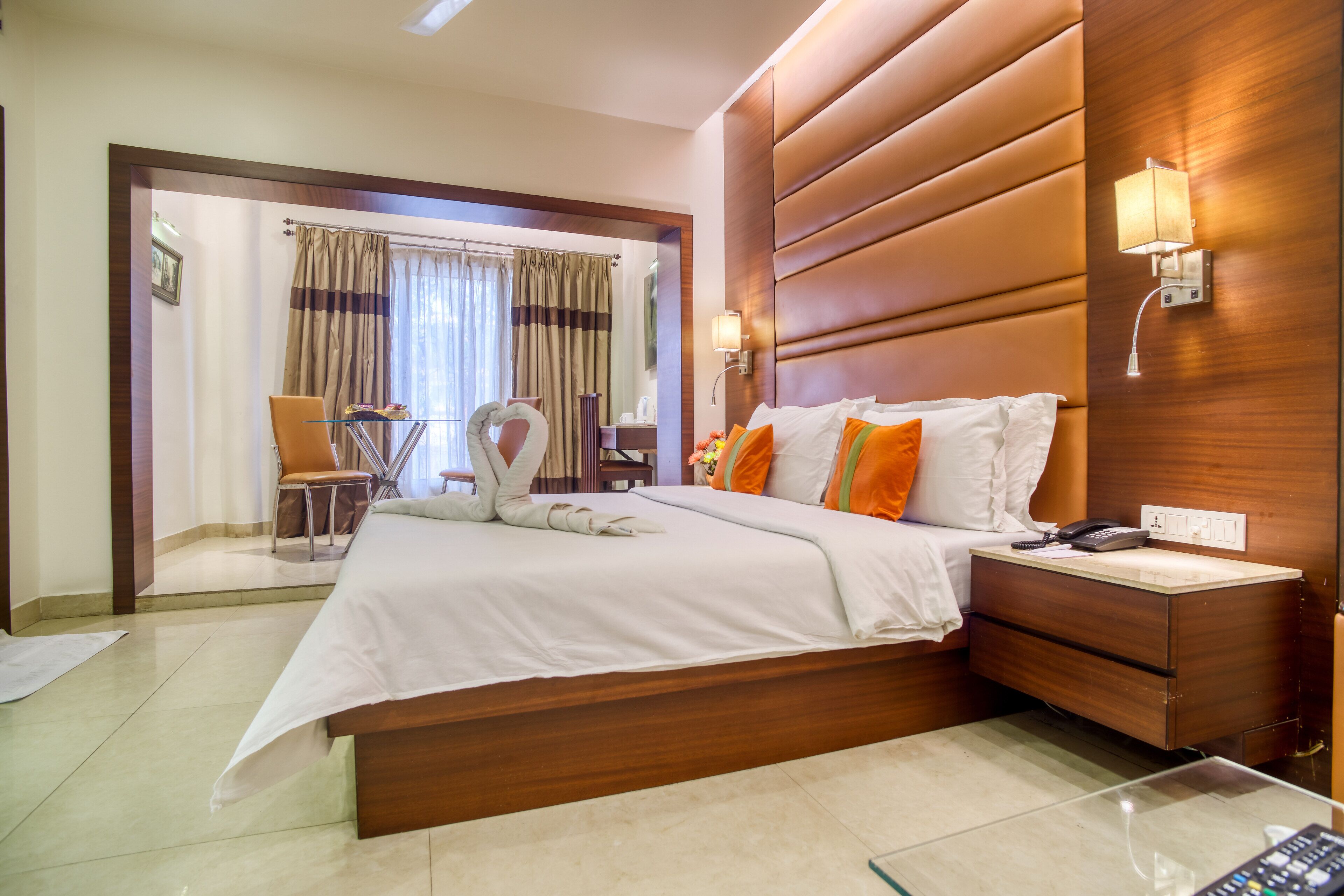 A hotel room with a large bed, a bedside table with a lamp, a chair, and a view of the bathroom through an open door.