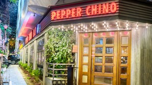 Een restaurant genaamd "Pepper Chino", met een neonreclame, houten deuren en een wand met potplanten.