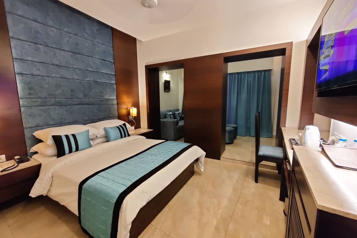 A hotel room with a large bed, a desk, a TV, and a bathroom visible through an open door.