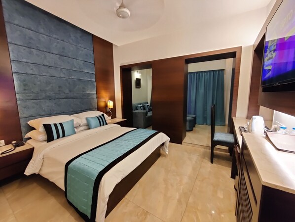 Habitación de hotel con una cama grande, un escritorio, un televisor y un baño visible a través de una puerta abierta.
