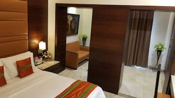 A hotel room with a large bed, a bedside table with a lamp, a small table with a vase of flowers, a sofa, and a chair.