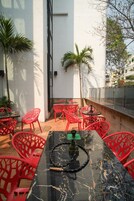 An outdoor seating area with red chairs and a black marble table, surrounded by white walls and palm trees.