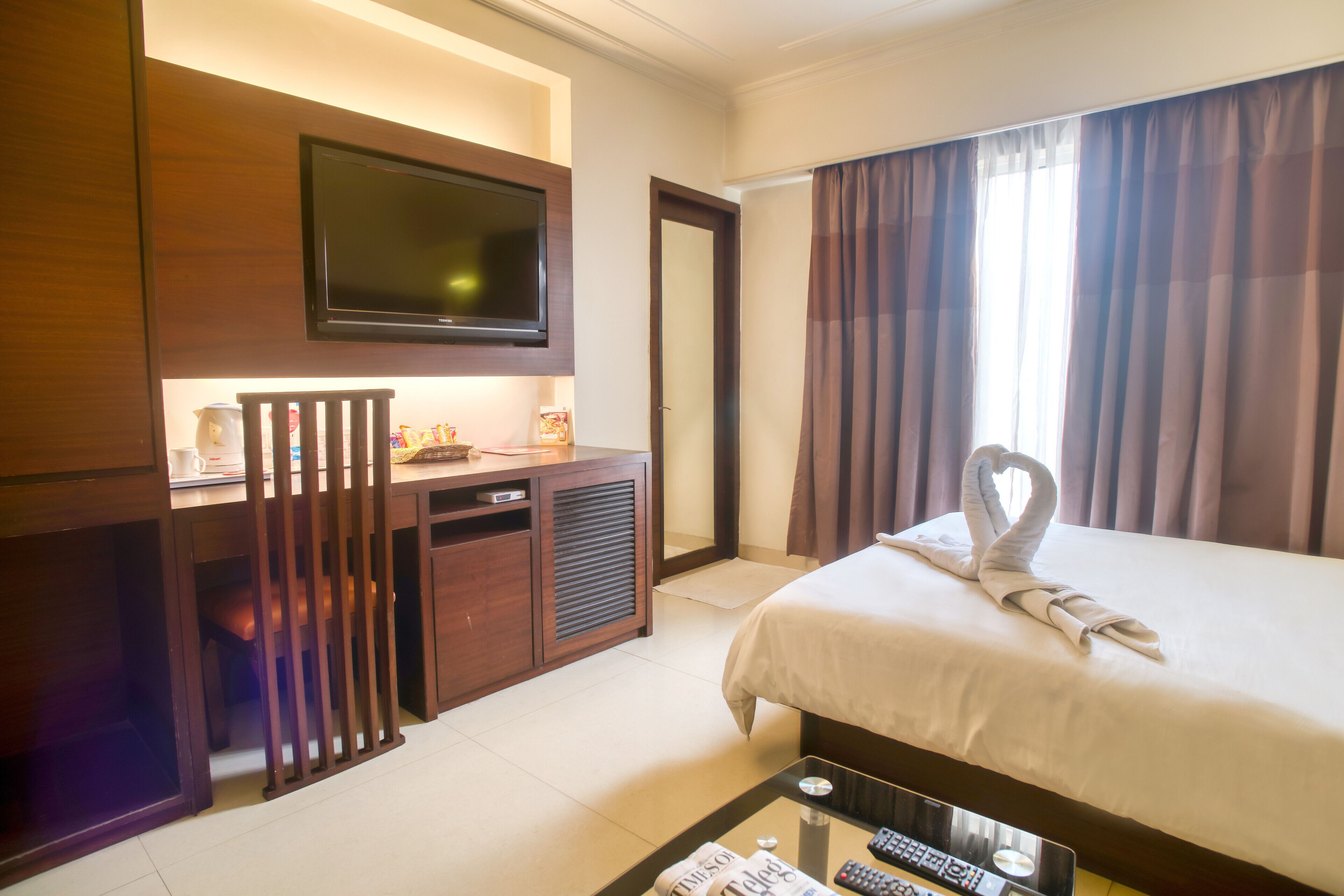 A hotel room with a bed, a desk, a television, and a window with curtains.