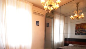 A hotel room with a large bed, a smaller bed, a chandelier, a painting on the wall, and a door with a mirror. - Venezianamente - Casa Cavaletti (Venice)