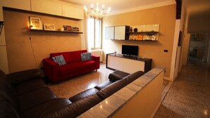 A living room with a red sofa, a brown leather couch, a TV, and a kitchen area with cabinets and a countertop. - Venezianamente - Casa Cavaletti (Venice)