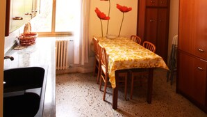 A compact kitchen with a dining table, chairs, a radiator, and a window with curtains. - Venezianamente - Casa Cavaletti (Venice)